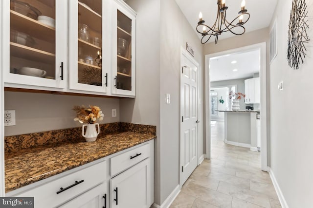 bar featuring dark stone countertops, a notable chandelier, pendant lighting, and white cabinets