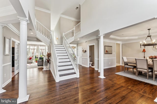 foyer featuring ornamental molding, dark hardwood / wood-style floors, a chandelier, and ornate columns