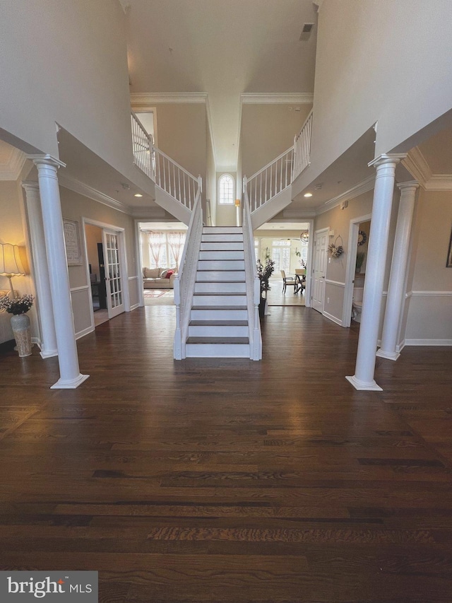 interior space with dark wood-type flooring, crown molding, decorative columns, and a high ceiling