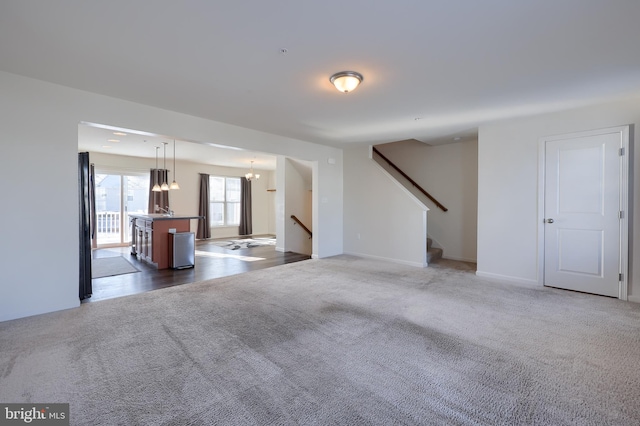 unfurnished living room with an inviting chandelier and dark carpet