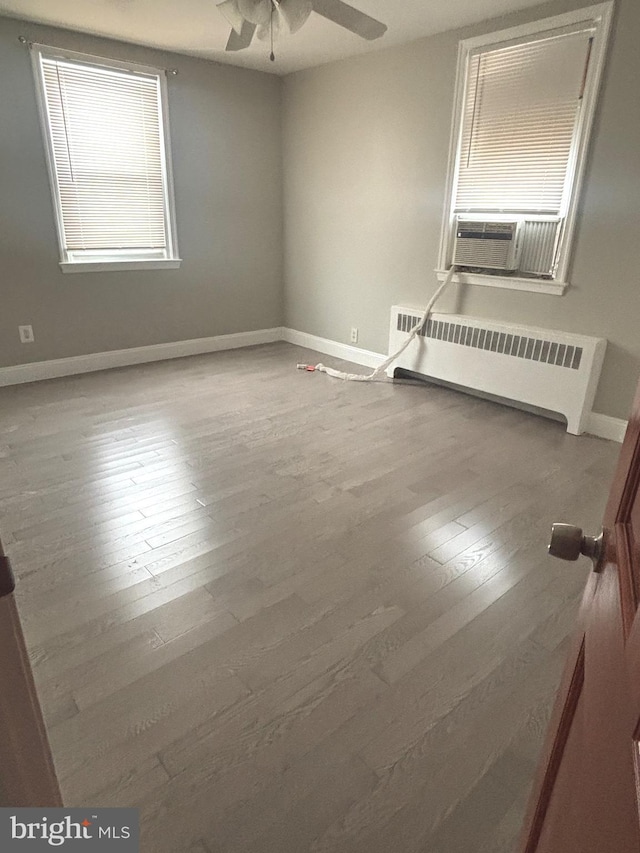 empty room featuring wood-type flooring, radiator, cooling unit, and ceiling fan