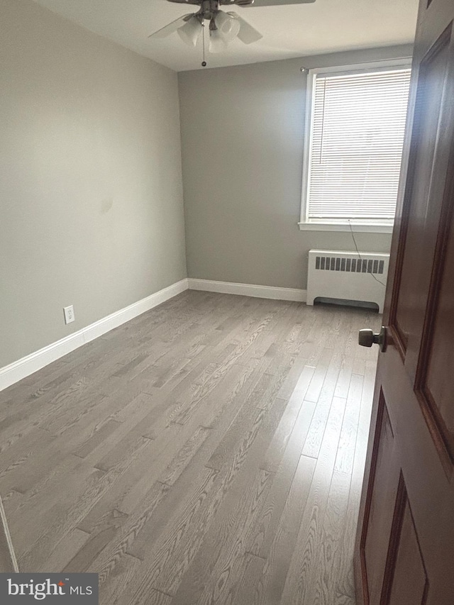 empty room featuring ceiling fan, radiator heating unit, and light wood-type flooring