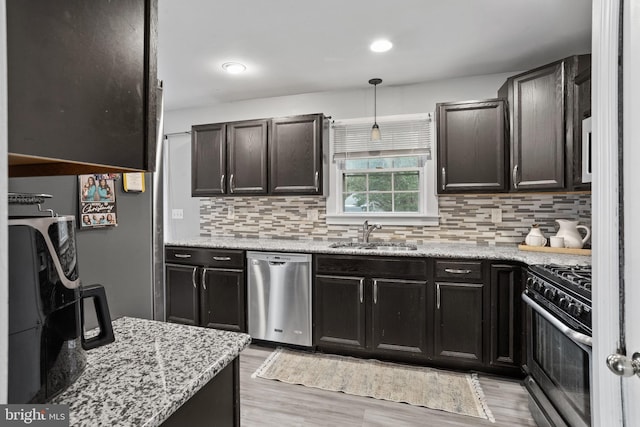 kitchen with appliances with stainless steel finishes, sink, backsplash, hanging light fixtures, and light hardwood / wood-style floors