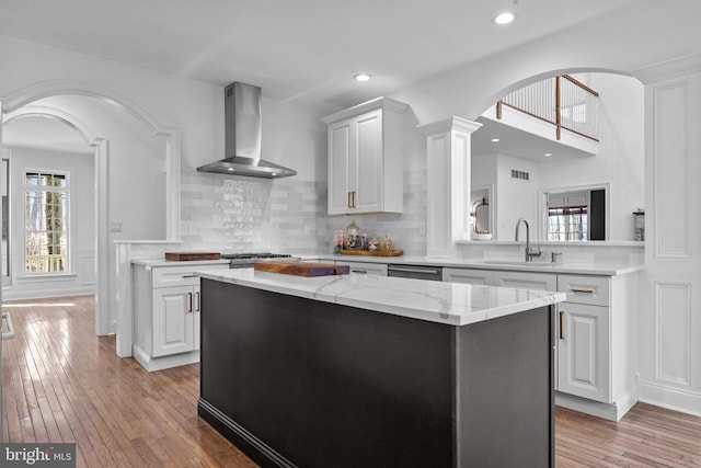 kitchen with wall chimney exhaust hood, sink, light stone counters, a center island, and white cabinets