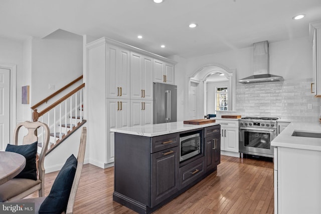 kitchen with hardwood / wood-style flooring, white cabinetry, a center island, high end appliances, and wall chimney exhaust hood