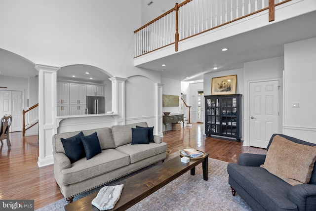 living room with decorative columns, wood-type flooring, and a high ceiling