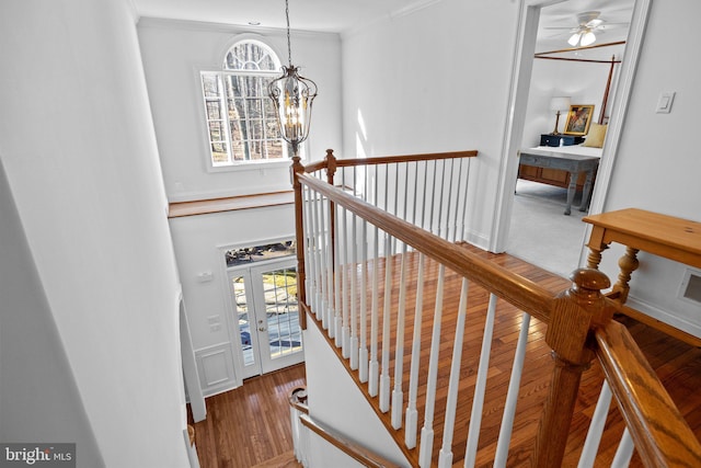 stairs with an inviting chandelier, hardwood / wood-style floors, a wealth of natural light, and ornamental molding