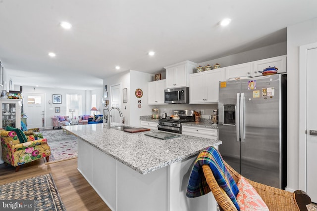 kitchen with sink, white cabinetry, light stone counters, stainless steel appliances, and a kitchen island with sink