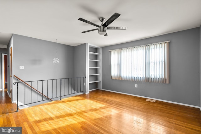 unfurnished room with hardwood / wood-style flooring, ceiling fan with notable chandelier, and built in shelves