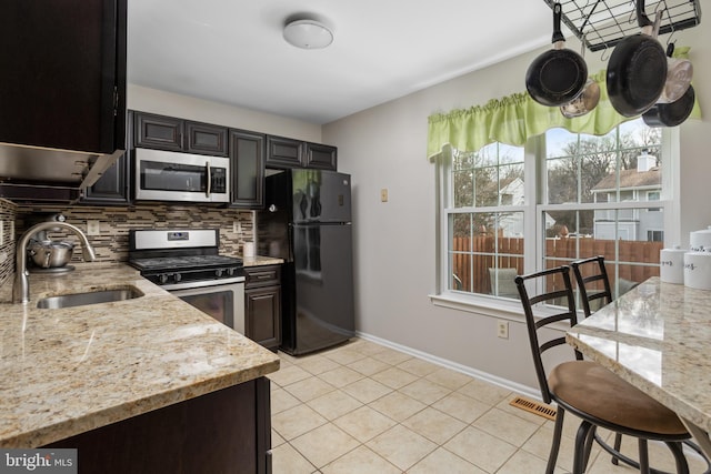 kitchen with tasteful backsplash, sink, light tile patterned floors, stainless steel appliances, and light stone countertops