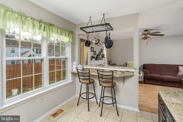 kitchen with a breakfast bar, kitchen peninsula, light stone countertops, and light tile patterned floors