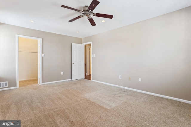 unfurnished bedroom with a walk in closet, a closet, ceiling fan, and carpet flooring