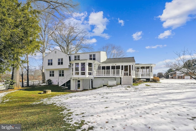 snow covered back of property with a yard and a sunroom