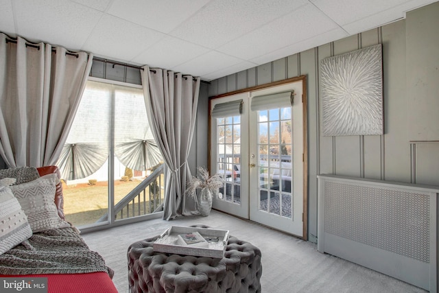 living area with french doors, light colored carpet, radiator heating unit, and a paneled ceiling