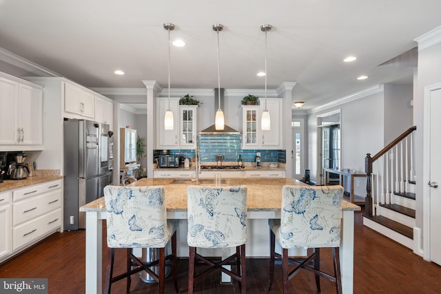 kitchen with wall chimney range hood, stainless steel appliances, backsplash, ornamental molding, and glass insert cabinets