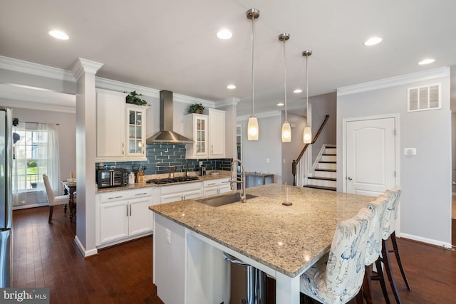 kitchen with gas cooktop, a sink, wall chimney exhaust hood, visible vents, and a center island with sink