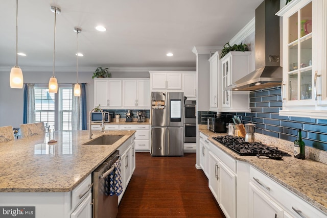 kitchen with wall chimney range hood, crown molding, appliances with stainless steel finishes, and a sink
