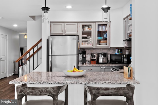 kitchen with a breakfast bar area, light stone counters, hanging light fixtures, stainless steel fridge, and backsplash