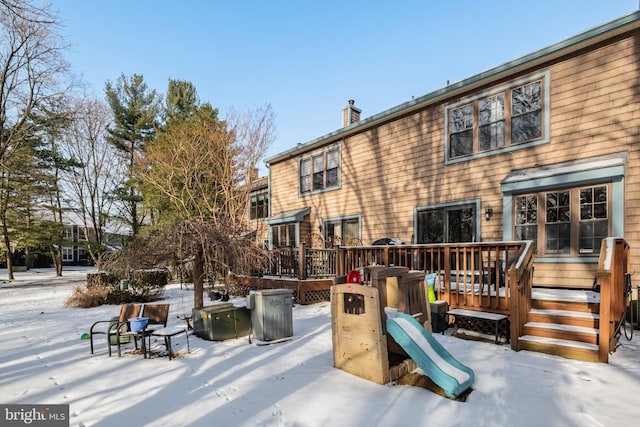 snow covered back of property with a playground and a deck