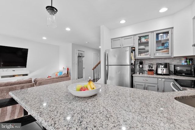 kitchen featuring a breakfast bar area, tasteful backsplash, stainless steel fridge, pendant lighting, and light stone countertops