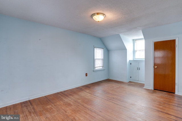 additional living space with lofted ceiling, a textured ceiling, and light hardwood / wood-style flooring