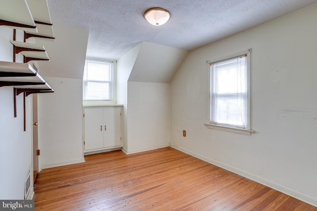 additional living space with lofted ceiling, light hardwood / wood-style floors, and a textured ceiling