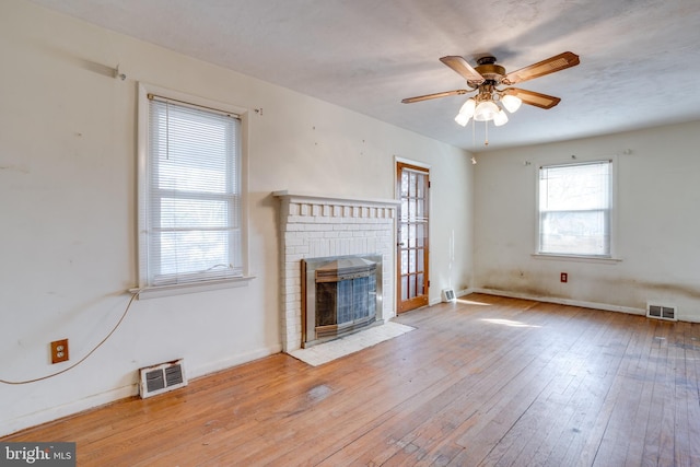 unfurnished living room with a brick fireplace, ceiling fan, and light wood-type flooring