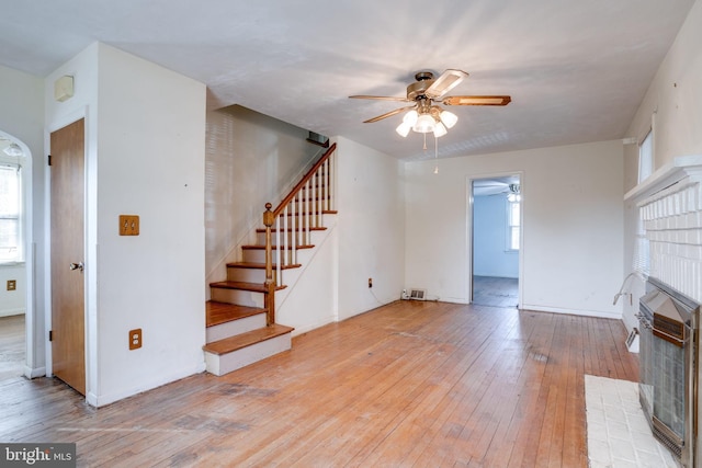 unfurnished living room with a tile fireplace, a wealth of natural light, ceiling fan, and light wood-type flooring