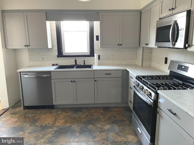 kitchen with sink, appliances with stainless steel finishes, gray cabinets, light stone countertops, and backsplash