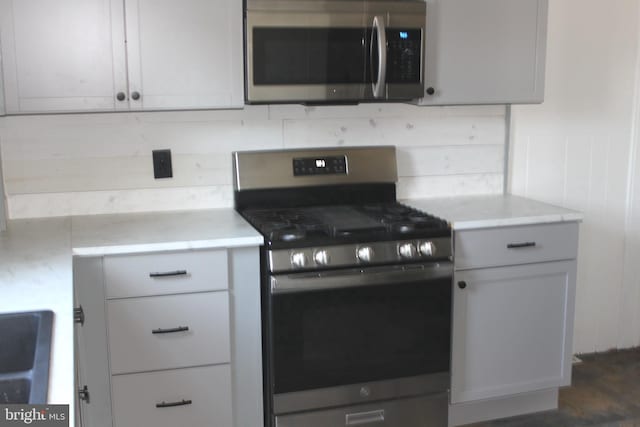 kitchen featuring stainless steel appliances, sink, gray cabinetry, and wooden walls