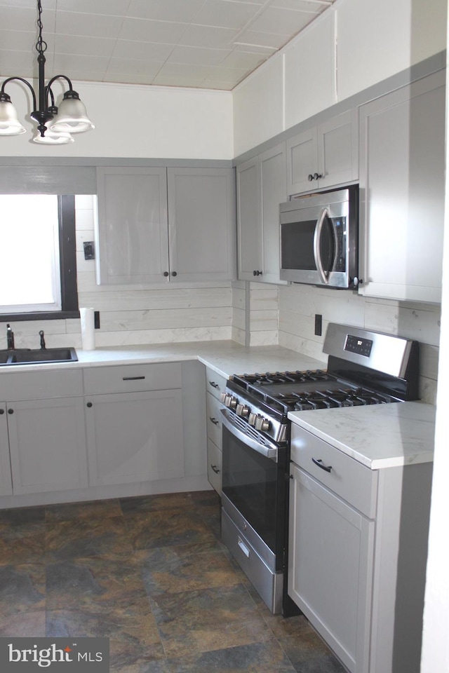 kitchen with appliances with stainless steel finishes, pendant lighting, sink, gray cabinetry, and a notable chandelier