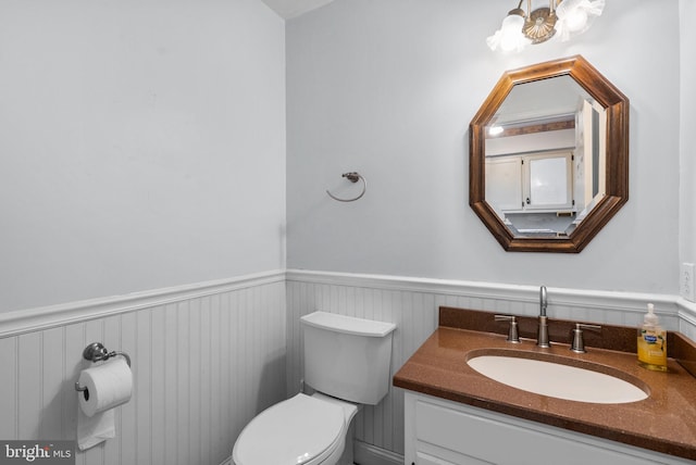 bathroom with toilet, an inviting chandelier, vanity, and wainscoting