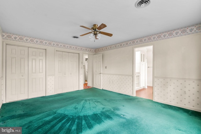 unfurnished bedroom featuring multiple closets, a wainscoted wall, visible vents, and wallpapered walls