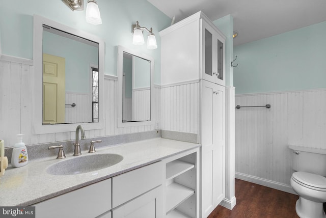 bathroom featuring a wainscoted wall, vanity, wood finished floors, and toilet