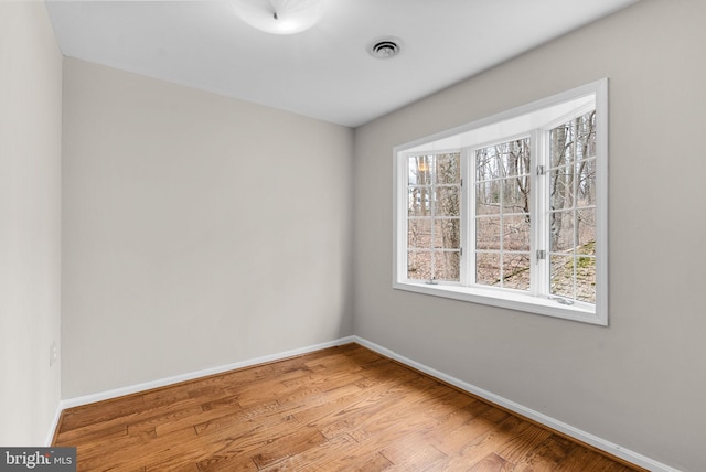 unfurnished room featuring baseboards, visible vents, and wood finished floors