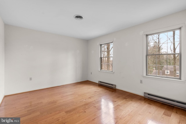 unfurnished room featuring a baseboard heating unit, light wood-style flooring, visible vents, and baseboards