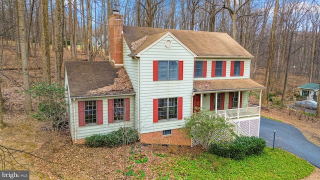 view of front of house featuring a shingled roof, covered porch, driveway, and a chimney