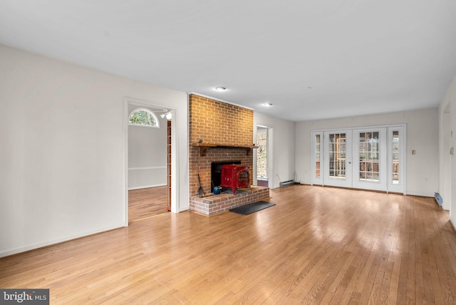 unfurnished living room with french doors, light wood finished floors, a wood stove, and baseboards