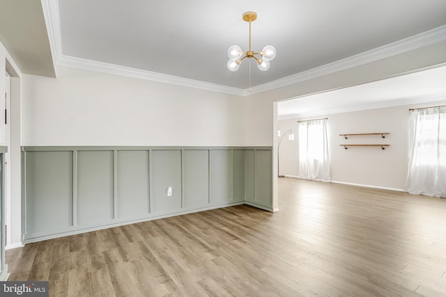 empty room with crown molding, a wealth of natural light, a chandelier, and light hardwood / wood-style floors