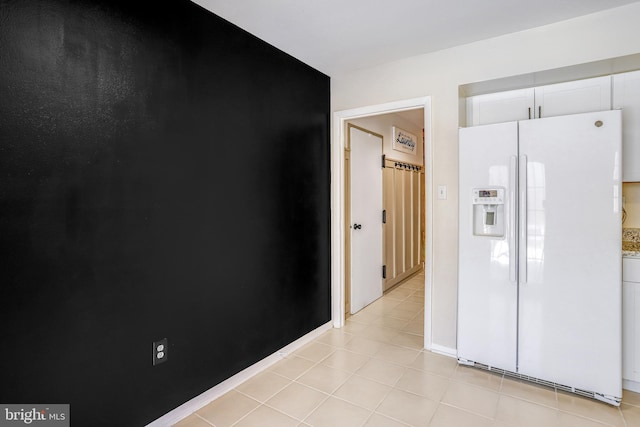 interior space featuring light stone countertops, white fridge with ice dispenser, light tile patterned floors, and white cabinets