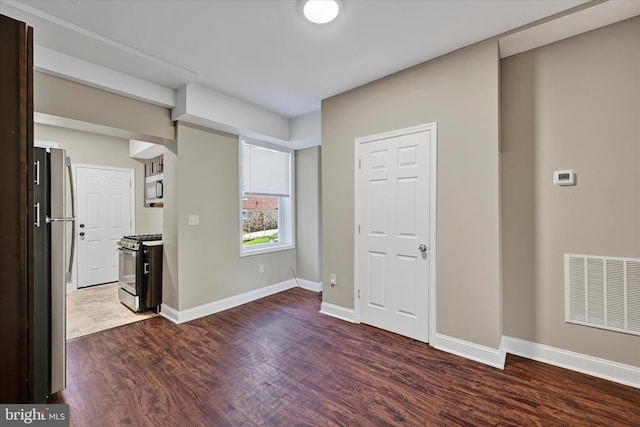 unfurnished bedroom featuring stainless steel fridge and dark hardwood / wood-style floors