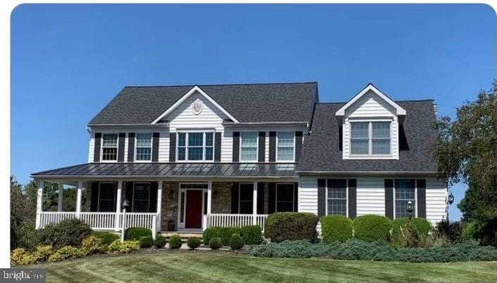 view of front facade with a standing seam roof, stone siding, covered porch, a front yard, and metal roof