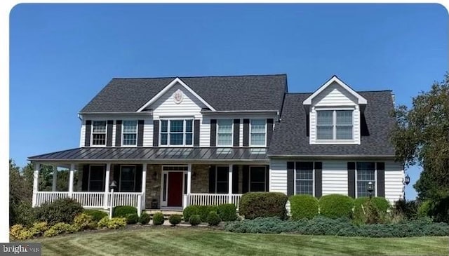 view of front facade featuring a standing seam roof, stone siding, a porch, a front yard, and metal roof