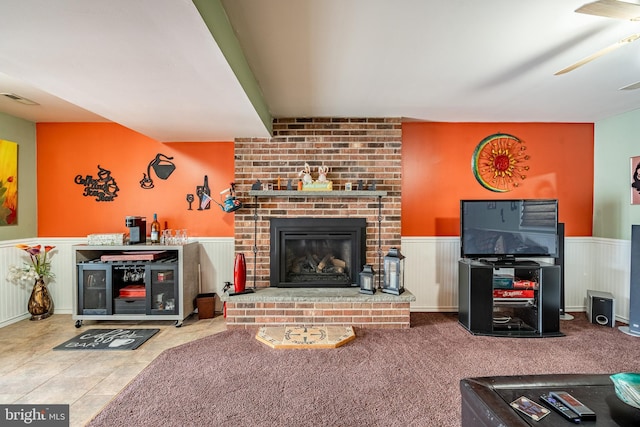 living room featuring visible vents, a ceiling fan, a wainscoted wall, and a fireplace