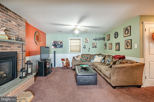 living room with carpet floors, a ceiling fan, wainscoting, and a fireplace