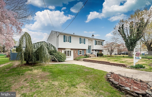 bi-level home featuring concrete driveway, brick siding, fence, and a front yard