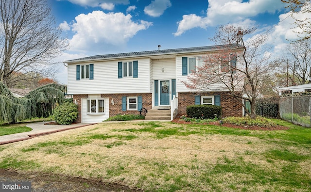 split foyer home featuring brick siding, fence, and a front lawn
