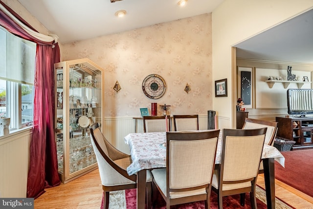 dining area featuring wallpapered walls, wood finished floors, and a wainscoted wall
