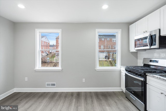 kitchen with appliances with stainless steel finishes, white cabinetry, light stone counters, a healthy amount of sunlight, and decorative backsplash