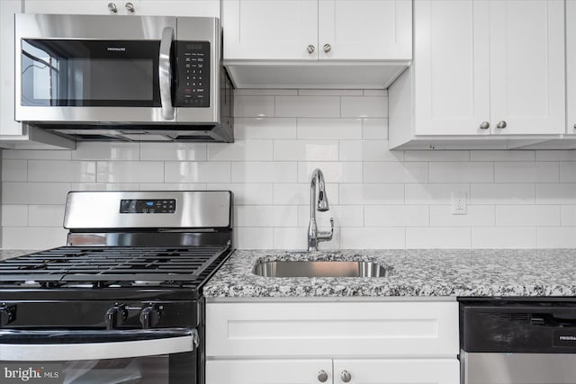 kitchen featuring appliances with stainless steel finishes, tasteful backsplash, white cabinetry, sink, and light stone counters